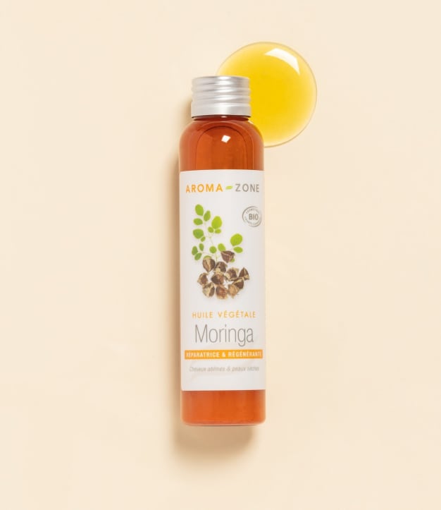 Huile de Moringa Aroma-Zone sur fond beige avec une goutte d'huile